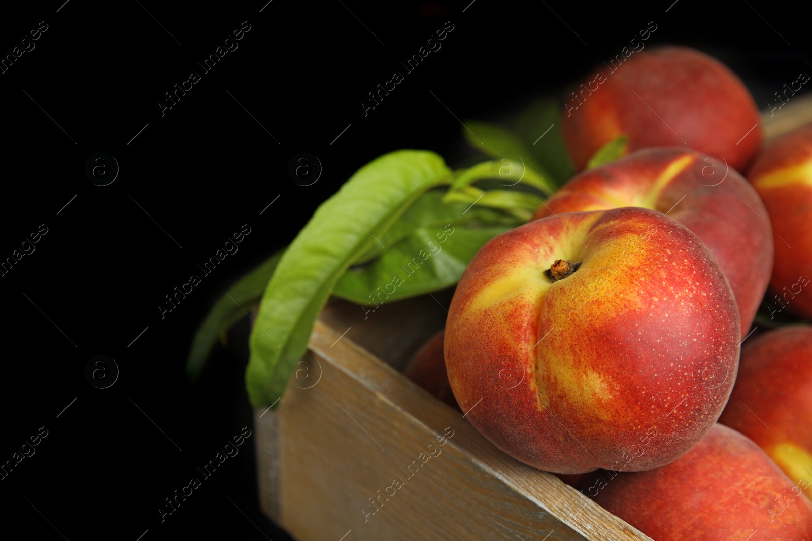 Photo of Wooden crate with tasty peaches and leaves on black background, closeup