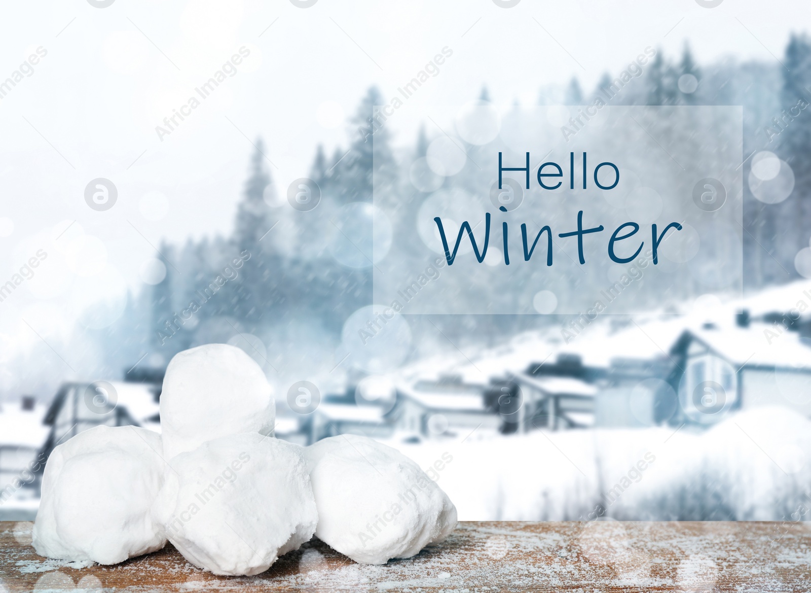 Image of Hello Winter. Snowballs on wooden surface and blurred view of houses near forest  