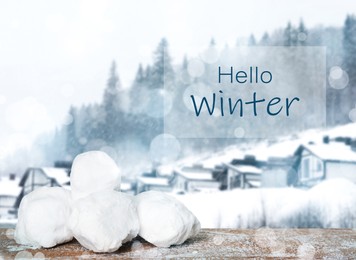 Image of Hello Winter. Snowballs on wooden surface and blurred view of houses near forest  