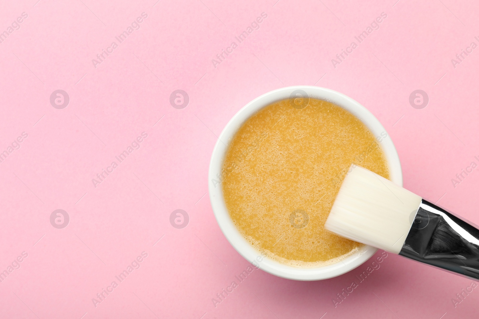 Photo of Bowl with handmade face mask and brush on pink background, top view. Space for text