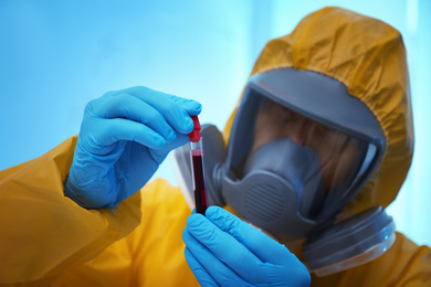 Photo of Scientist in chemical protective suit holding blood sample at laboratory, focus on test tube. Virus research