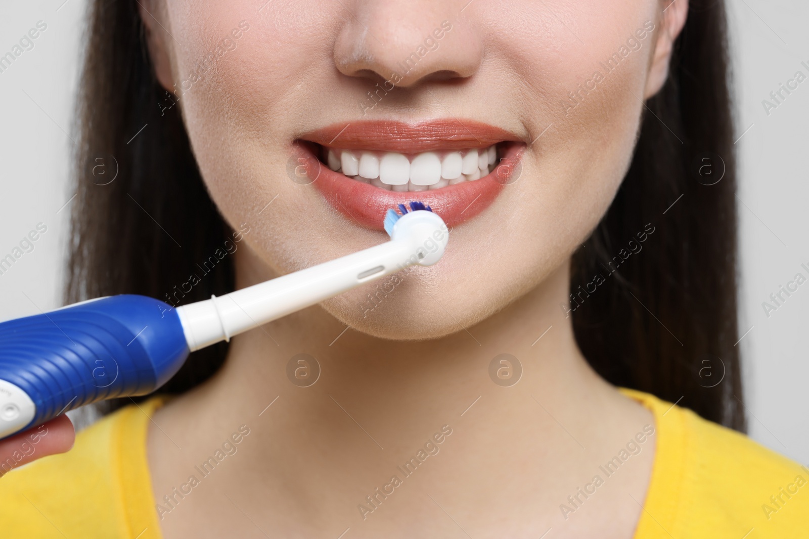 Photo of Woman brushing her teeth with electric toothbrush on white background, closeup