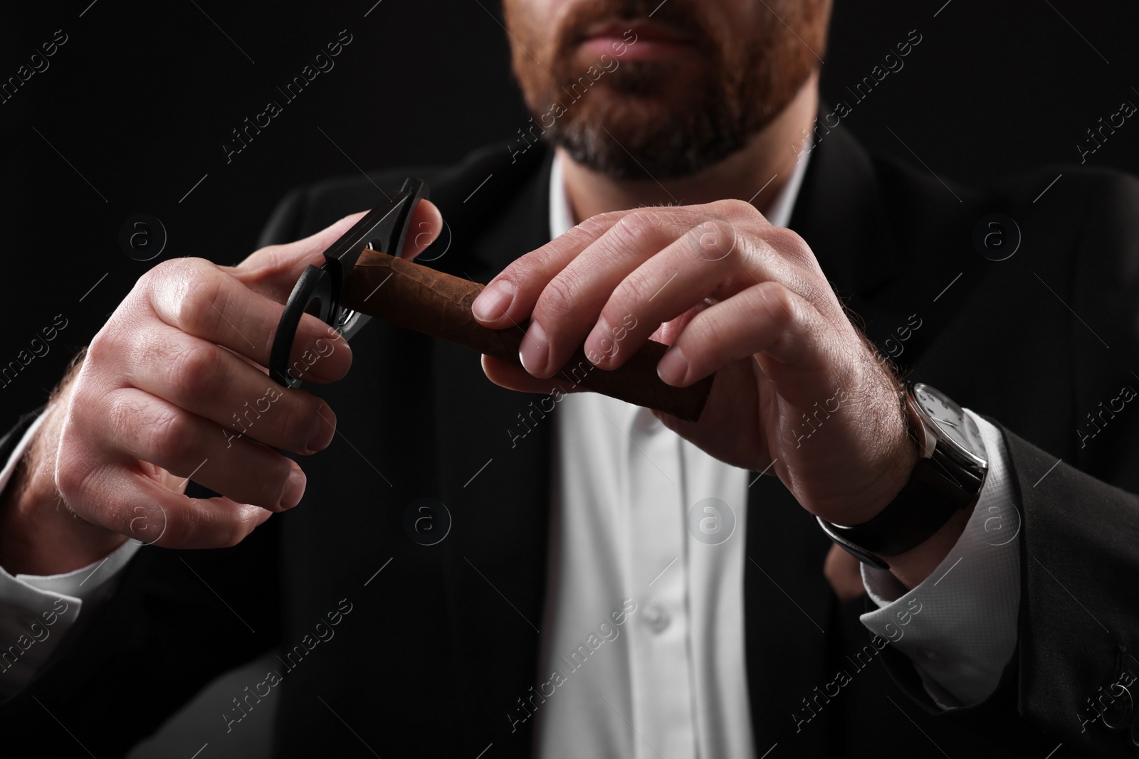 Photo of Man cutting tip of cigar on black background, closeup