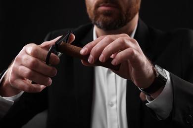 Photo of Man cutting tip of cigar on black background, closeup