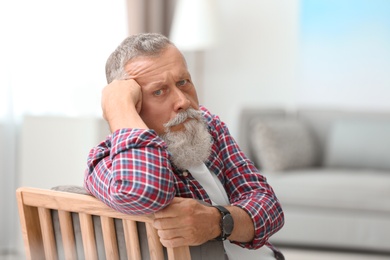 Portrait of handsome mature man sitting on chair in room