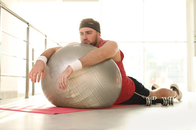 Lazy young man with exercise ball on yoga mat indoors