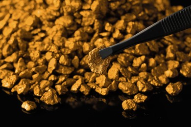 Tweezers with gold nugget above pile on black background, closeup