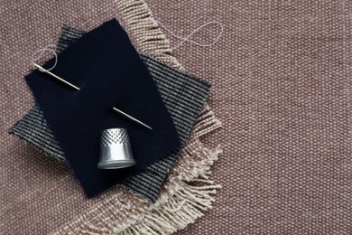 Photo of Silver thimble and needle on light brown cloth, flat lay with space for text. Sewing accessories