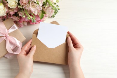 Photo of Happy Mother's Day. Woman holding envelope with blank card at white wooden table, top view