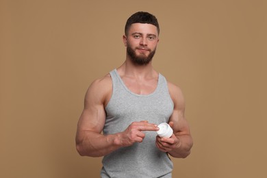 Photo of Handsome man applying body cream on pale brown background