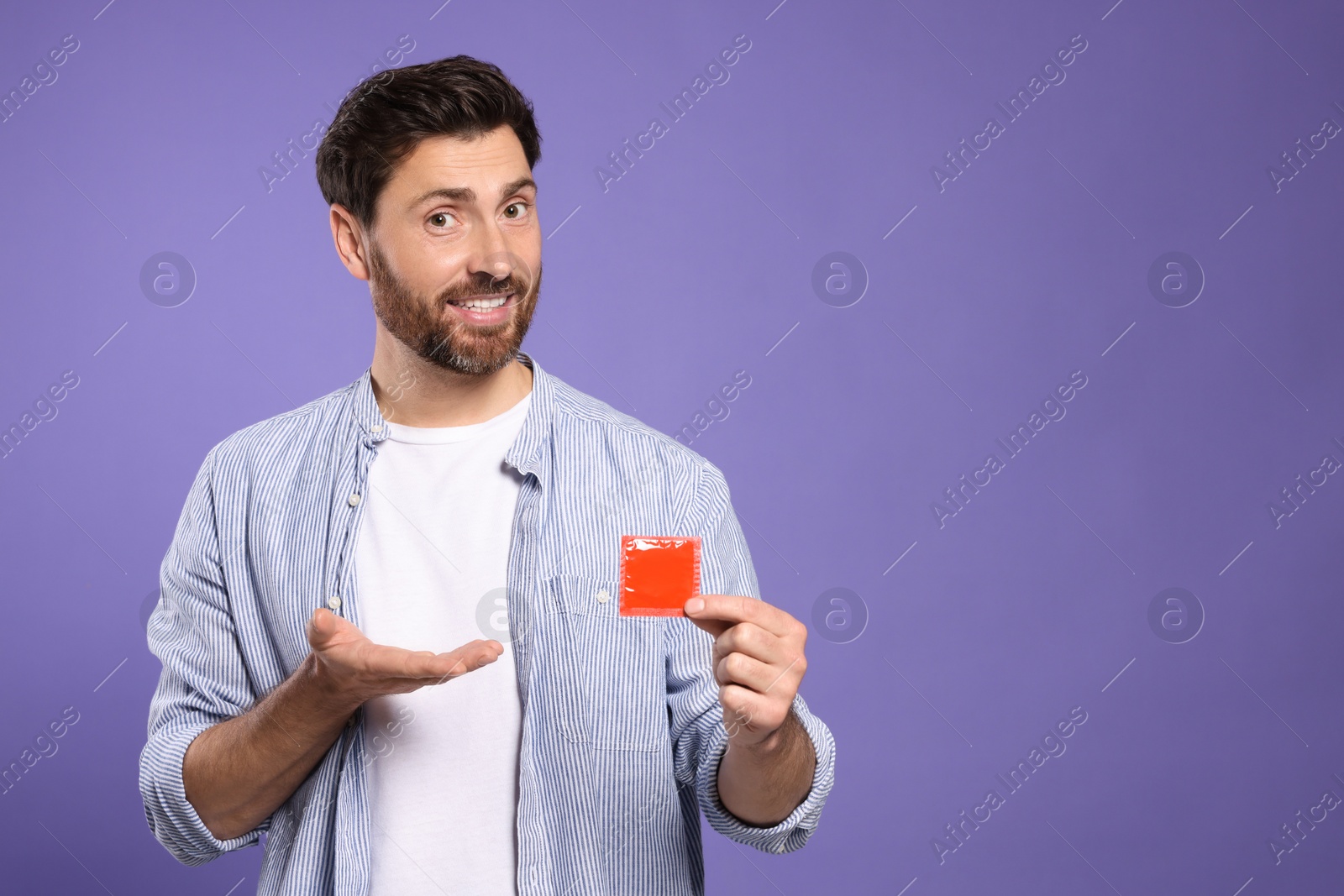 Photo of Man holding condom on purple background, space for text. Safe sex