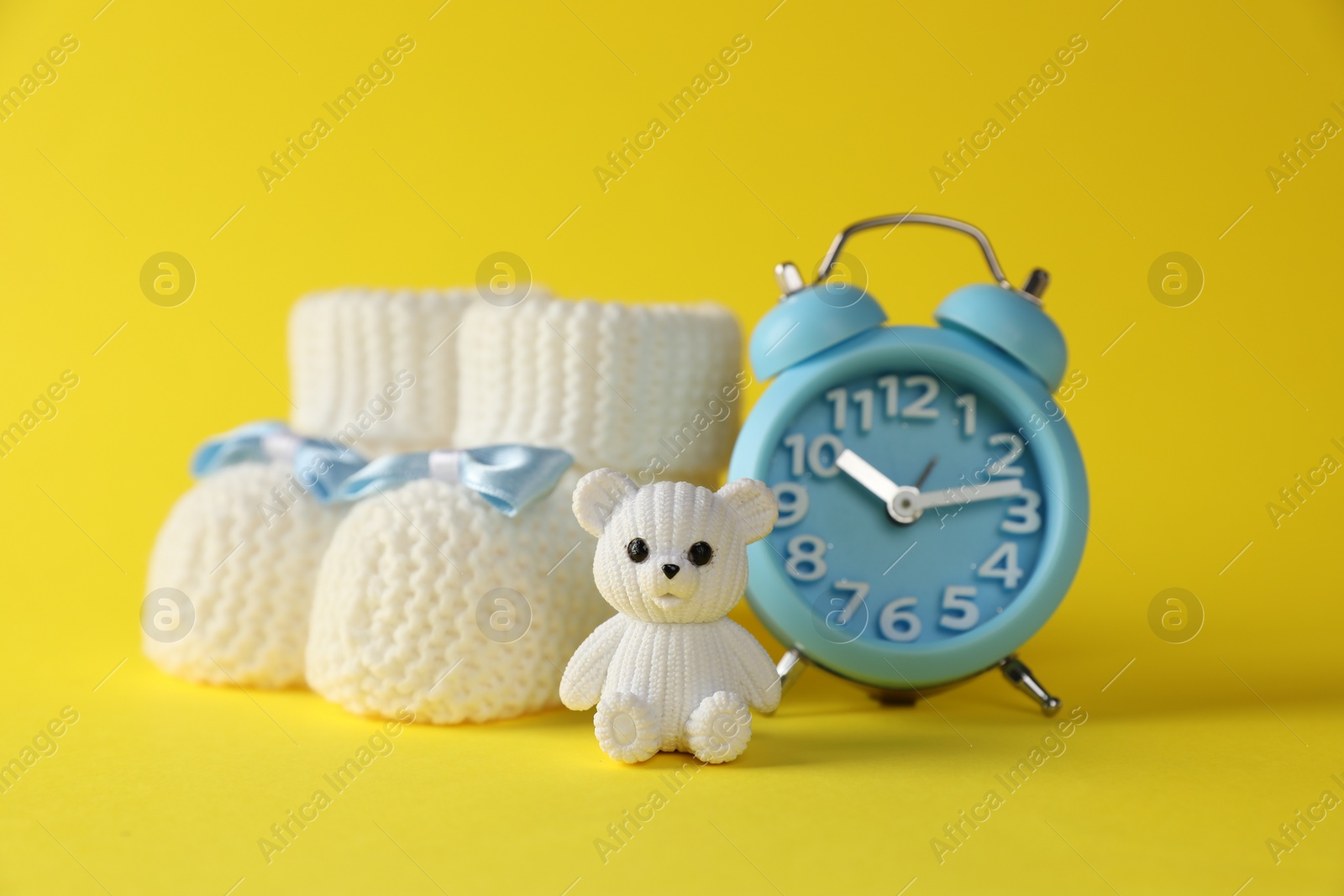 Photo of Alarm clock, toy bear and baby booties on yellow background. Time to give birth