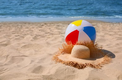Photo of Straw hat and beach ball near sea. Space for text