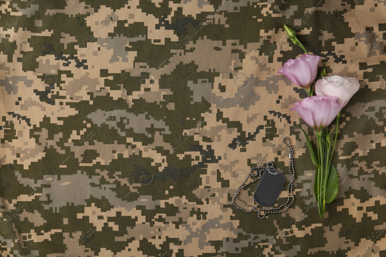 Photo of Fresh flowers and ID tag on camouflage background, flat lay with space for text. Armed Forces Day