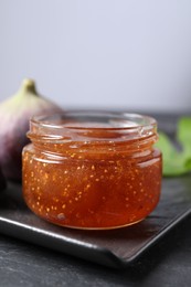 Jar of tasty fig jam on black table, closeup
