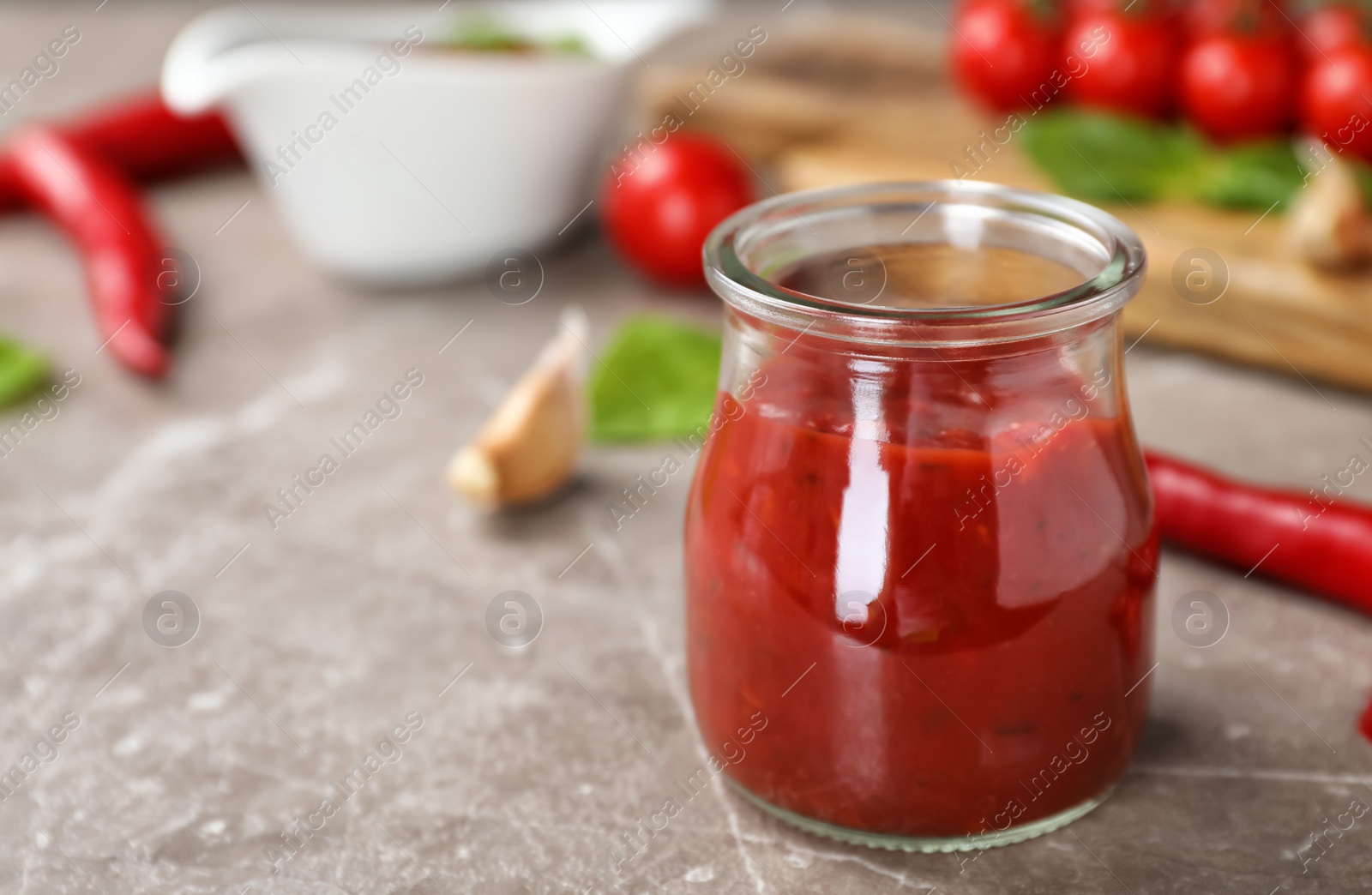 Photo of Jar with spicy chili sauce on gray table