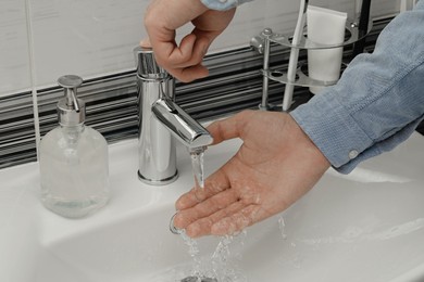 Photo of Man using water tap to wash hands in bathroom, closeup