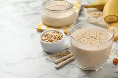 Photo of Glass of tasty banana smoothie with oatmeal on white marble table. Space for text