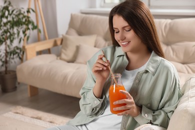 Photo of Beautiful young woman with glass bottle of juice on sofa at home