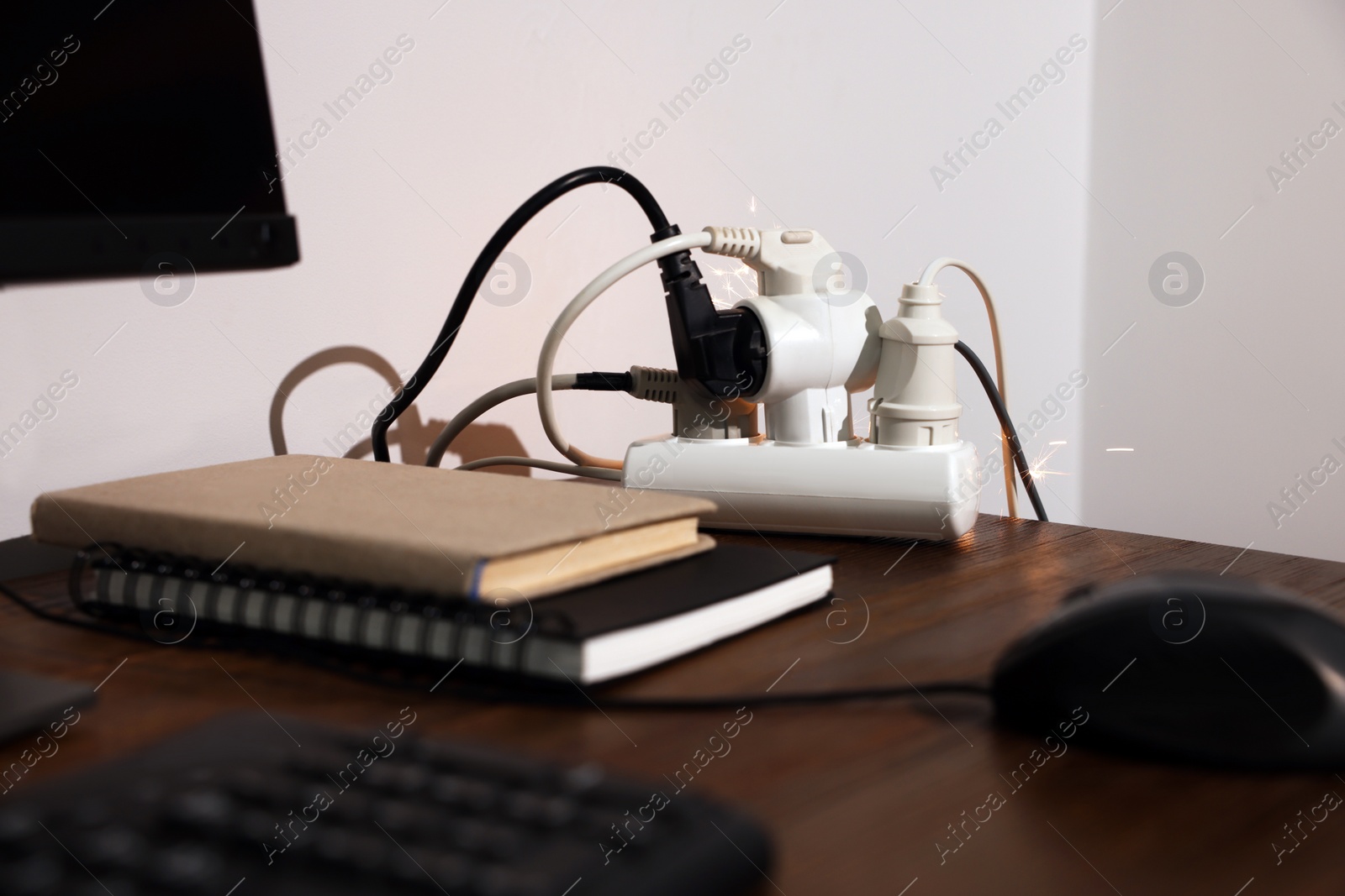 Photo of Inflamed plug in power strip indoors on wooden table. Electrical short circuit