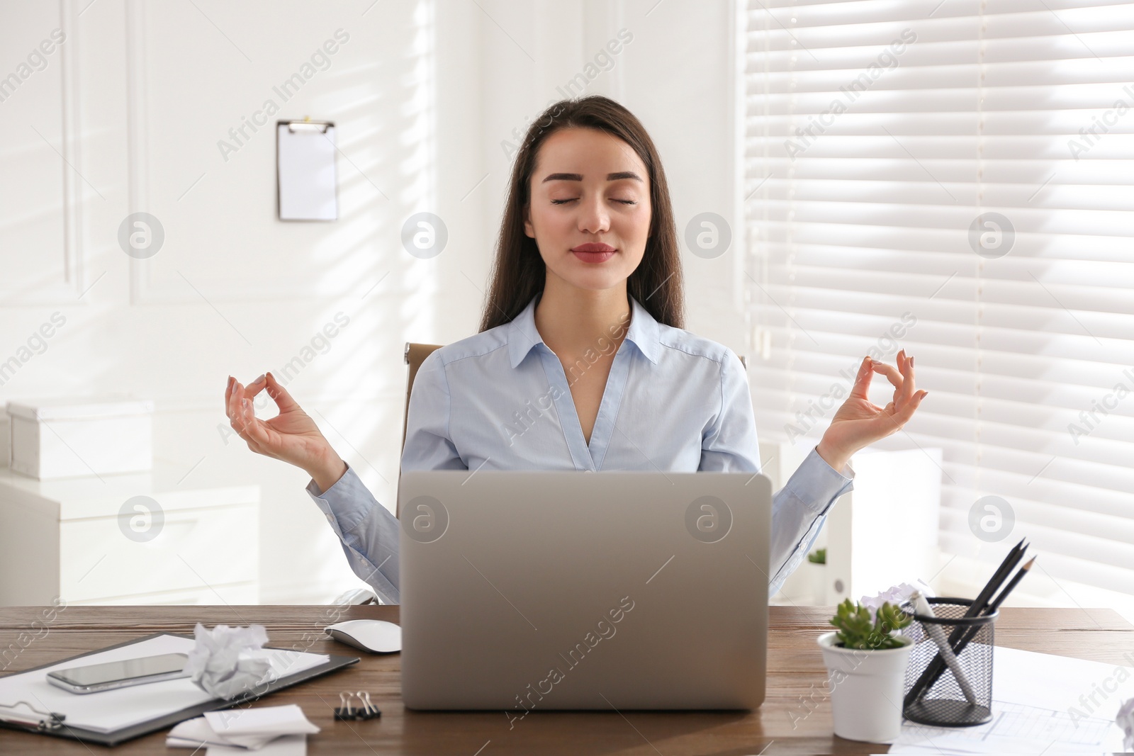 Photo of Businesswoman meditating at workplace in office. Stress relieving exercise