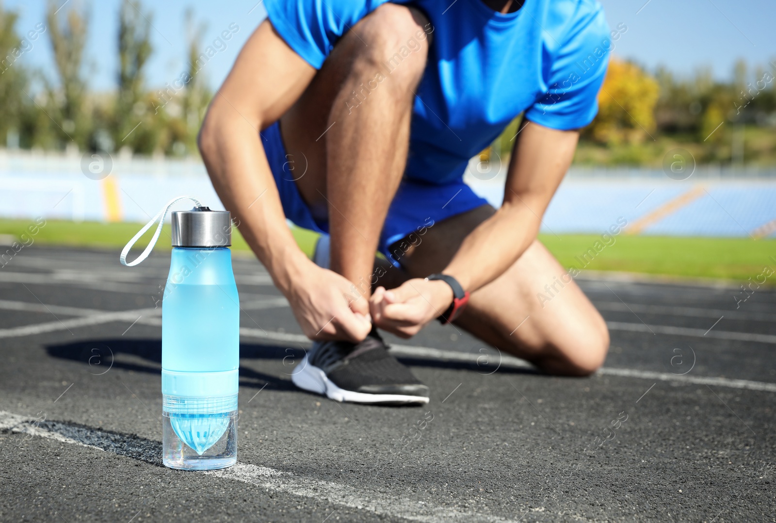 Photo of Sporty man tying shoelaces near bottle of water at stadium on sunny day