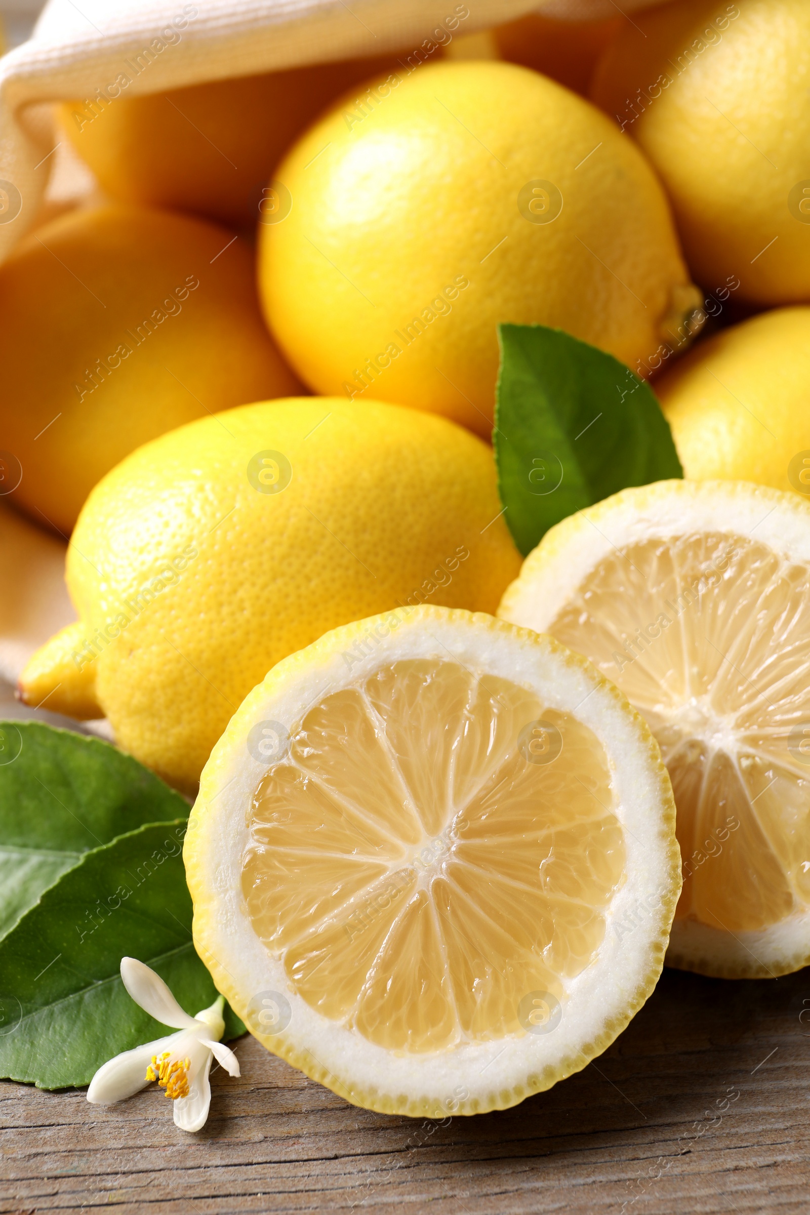 Photo of Many fresh ripe lemons with green leaves and flower on wooden table, closeup