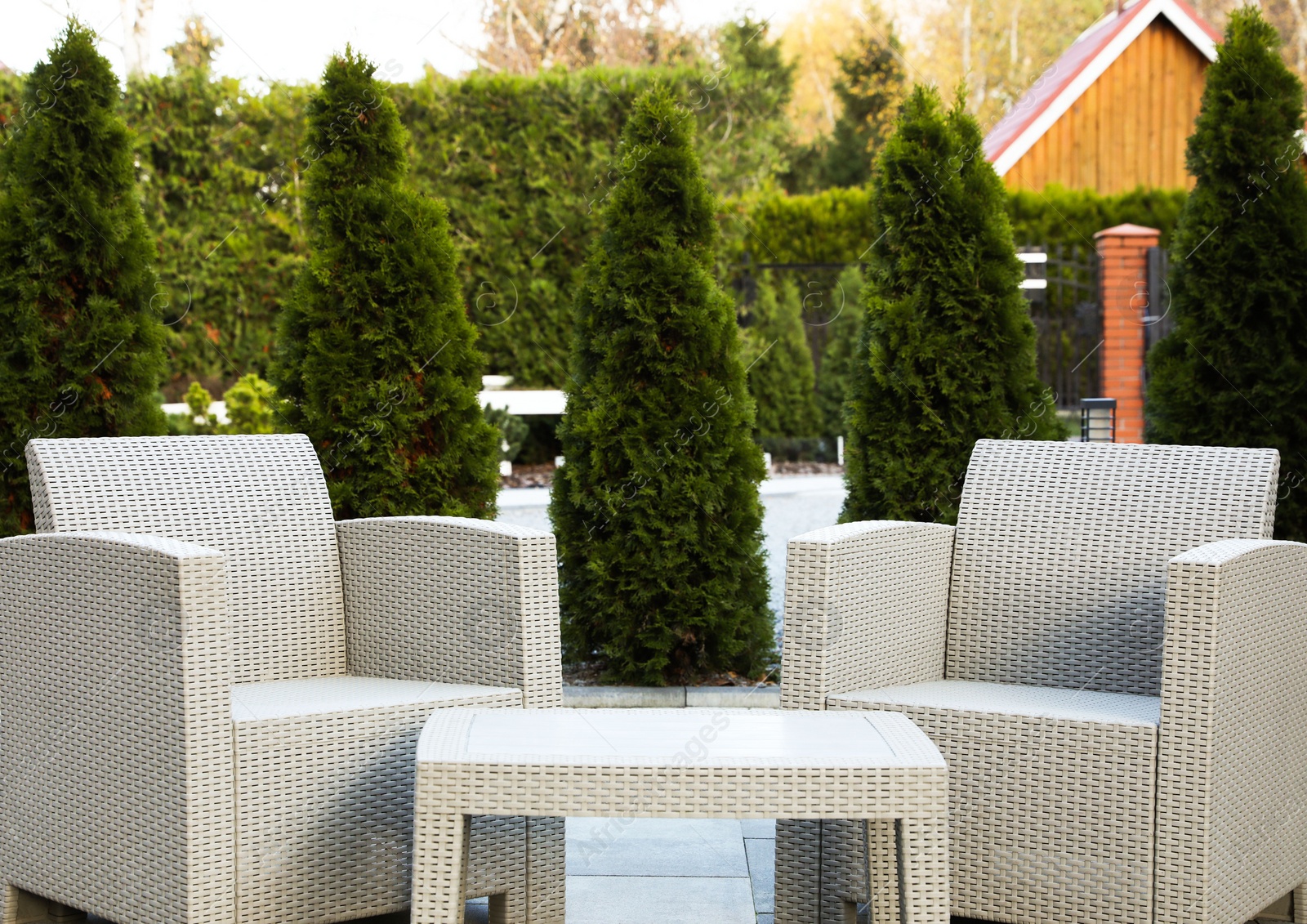 Photo of Comfortable armchairs and coffee table in backyard. Beautiful rattan garden furniture