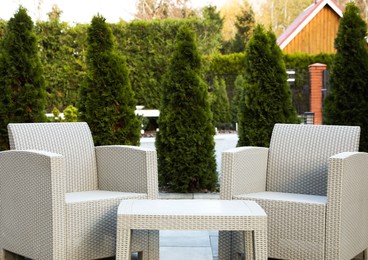 Photo of Comfortable armchairs and coffee table in backyard. Beautiful rattan garden furniture