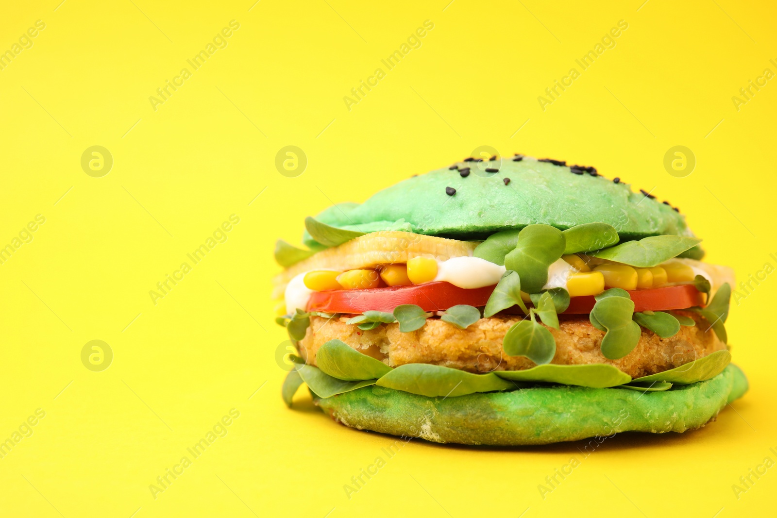 Photo of Tasty green vegan burger with vegetables, patty and microgreens on yellow background, closeup. Space for text