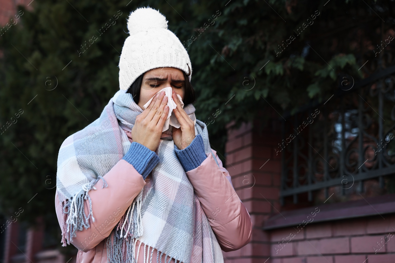 Photo of Woman with tissue blowing runny nose outdoors. Cold symptom