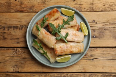 Plate with tasty fried spring rolls, arugula and lime on wooden table, top view