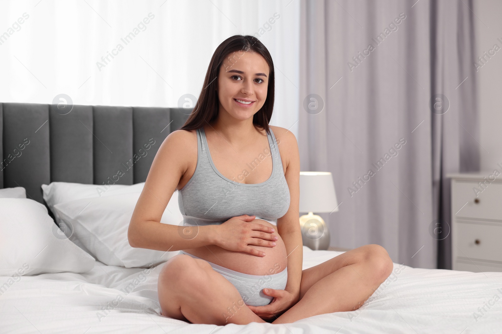 Photo of Beautiful pregnant woman in comfortable maternity underwear on bed at home