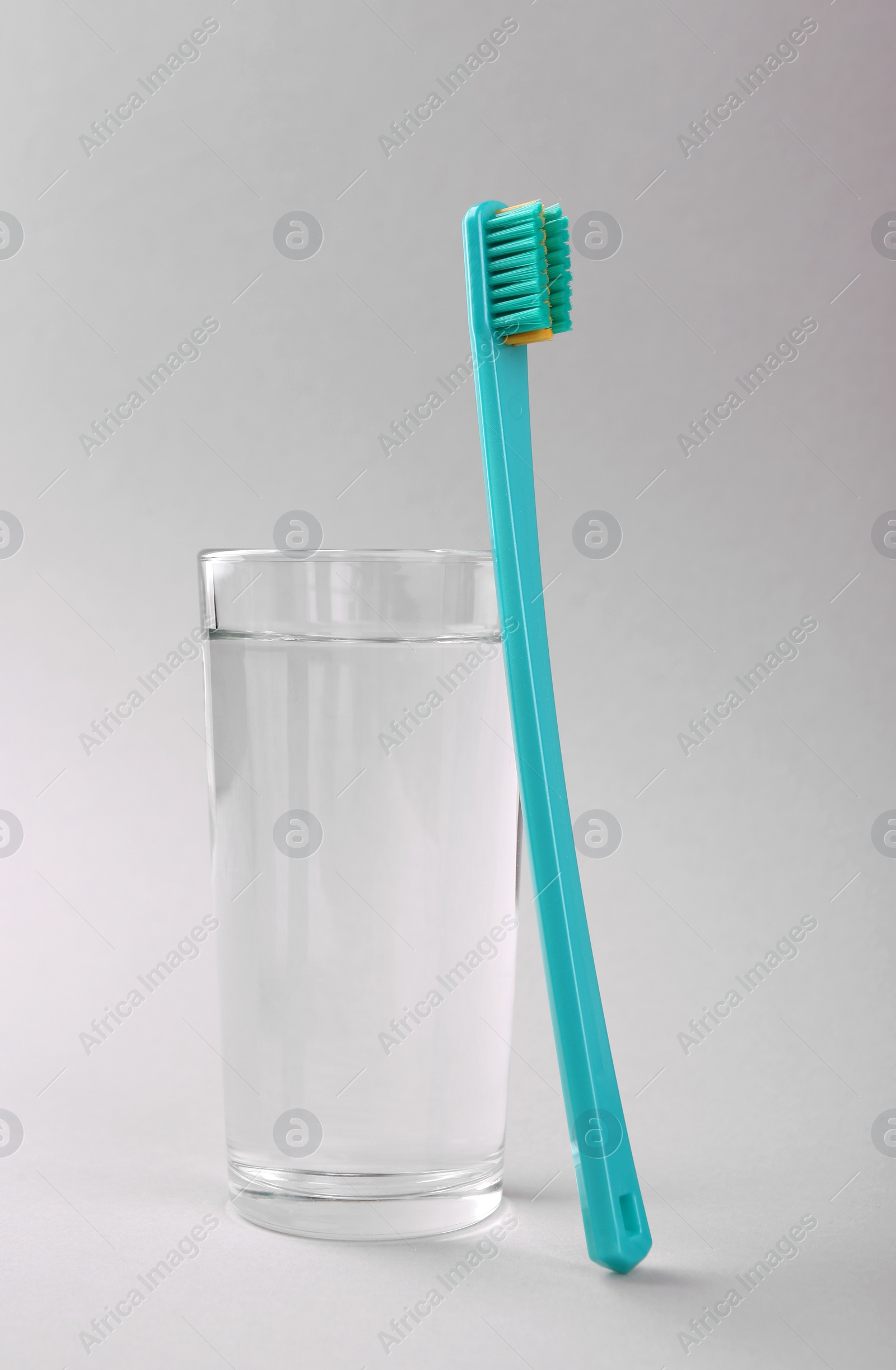 Photo of Plastic toothbrush and glass of water on light background