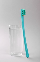 Plastic toothbrush and glass of water on light background