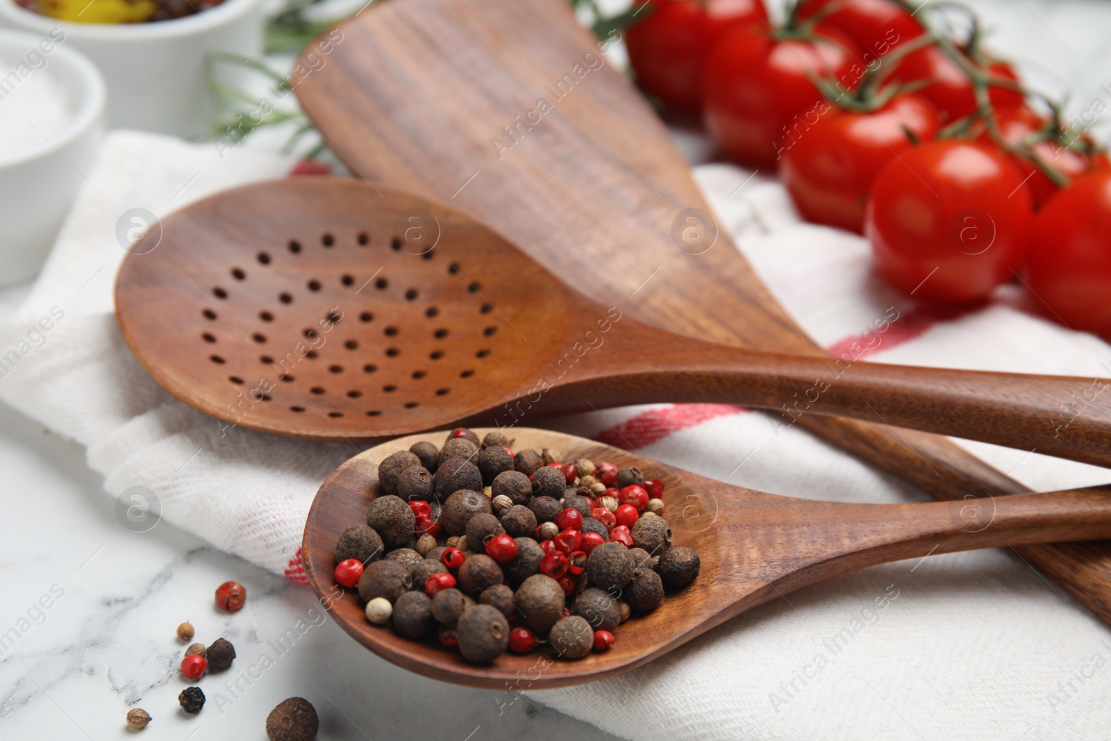Photo of Composition with wooden cooking utensils and peppercorns on white marble table, closeup