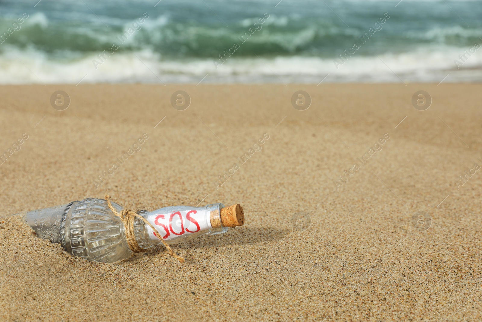 Photo of Glass bottle with SOS message on sand near sea, space for text