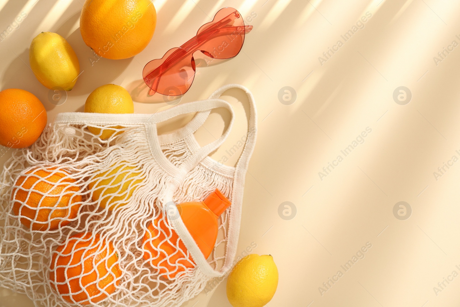 Photo of String bag with fresh fruits, sunscreen and sunglasses on beige background, flat lay. Space for text
