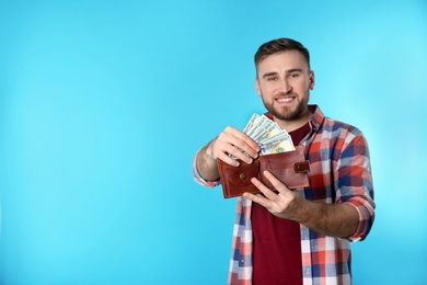 Photo of Happy young man putting money into wallet on color background. Space for text