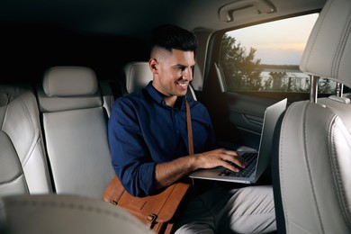 Photo of Businessman working on laptop in modern taxi