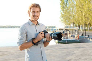 Photo of Handsome male photographer holding professional camera at pier. Space for text