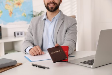 Photo of Happy manager holding passports at desk in travel agency, closeup