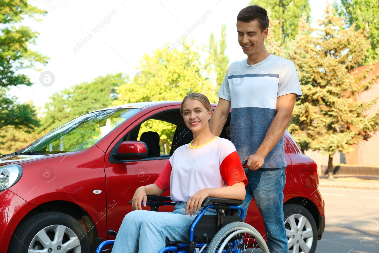 Photo of Young man with disabled woman in wheelchair near car outdoors