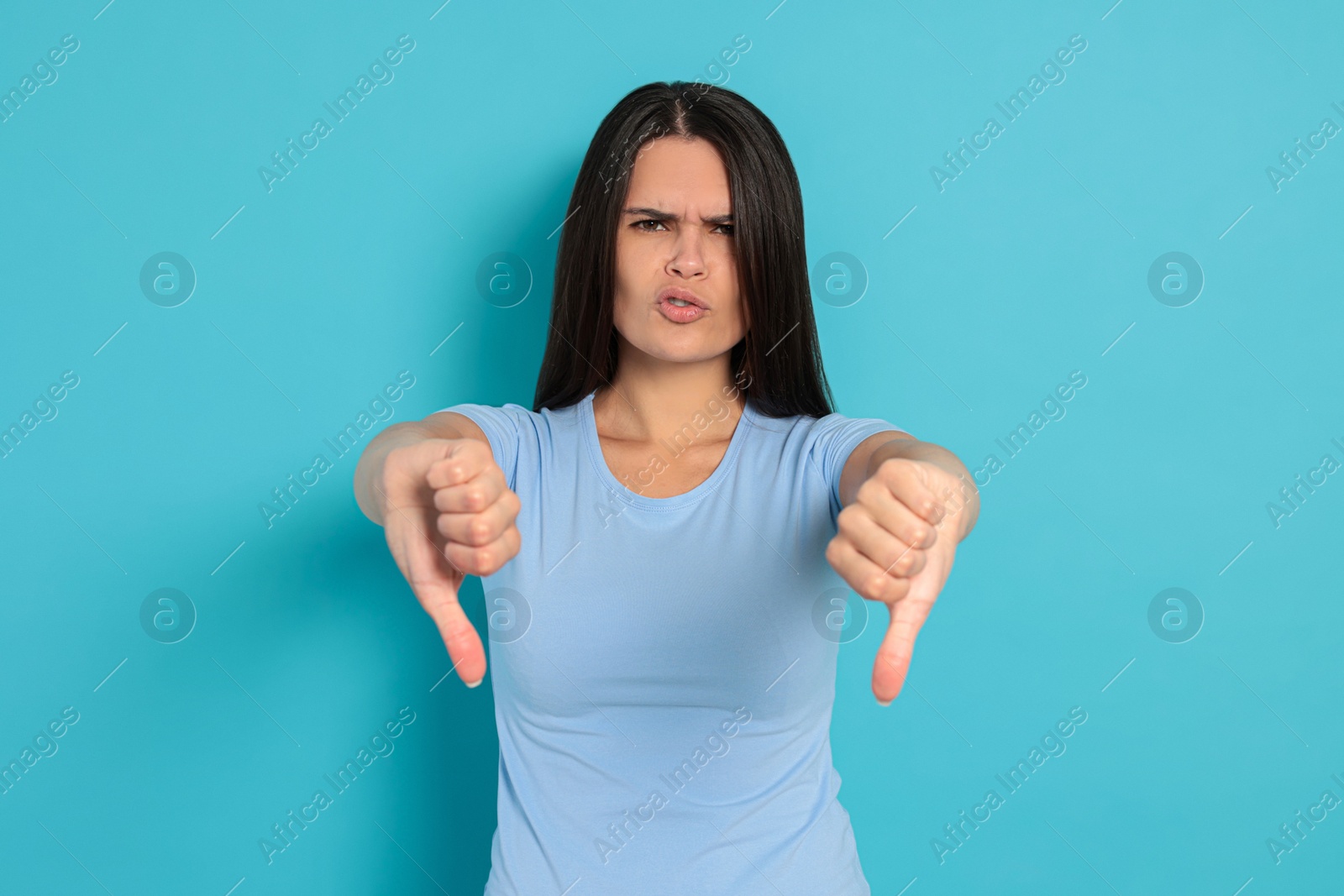 Photo of Young woman showing thumbs down on light blue background