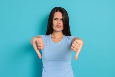 Young woman showing thumbs down on light blue background