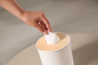 Woman taking paper tissue out of box on light table, closeup