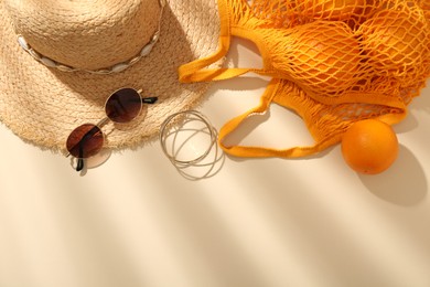 Photo of String bag with sunglasses, oranges and summer accessories on beige background, flat lay. Space for text