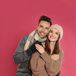 Photo of Happy young couple in warm clothes on pink background. Winter season