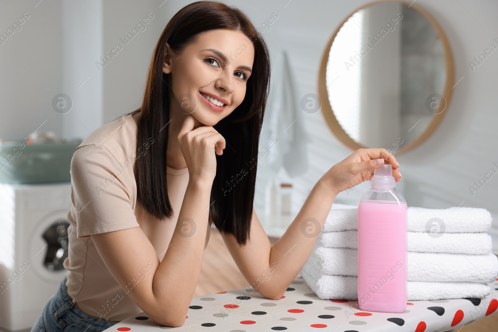 Photo of Woman near clean towels and fabric softener in bathroom