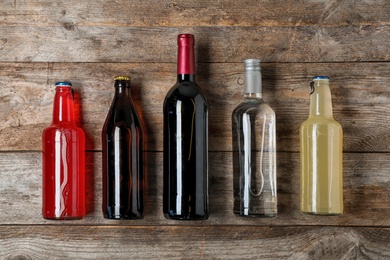 Bottles with different alcoholic drinks on wooden background, top view